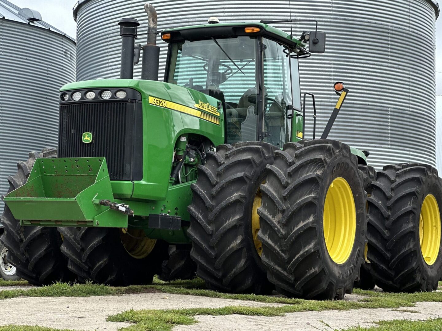 A large green tractor parked in front of some silos.