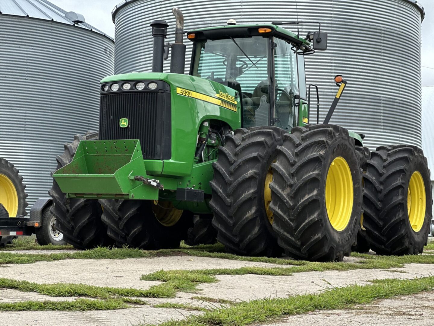 A large green tractor parked in front of some grain bins.